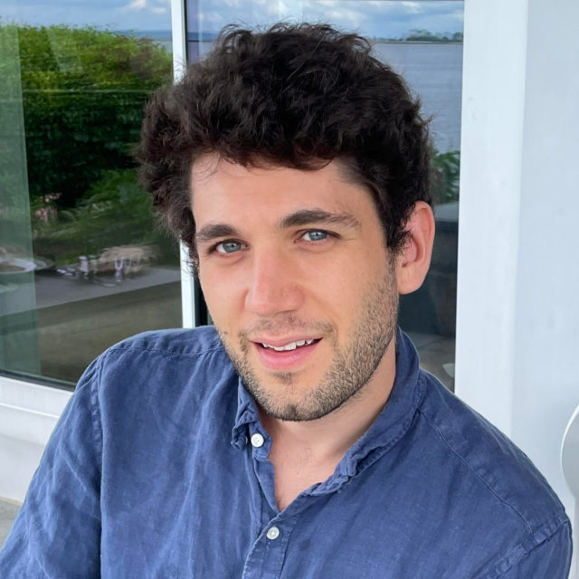 CDT staff member Gabriel Nicholas. Wearing a blue collared shirt, in front of a glass window.