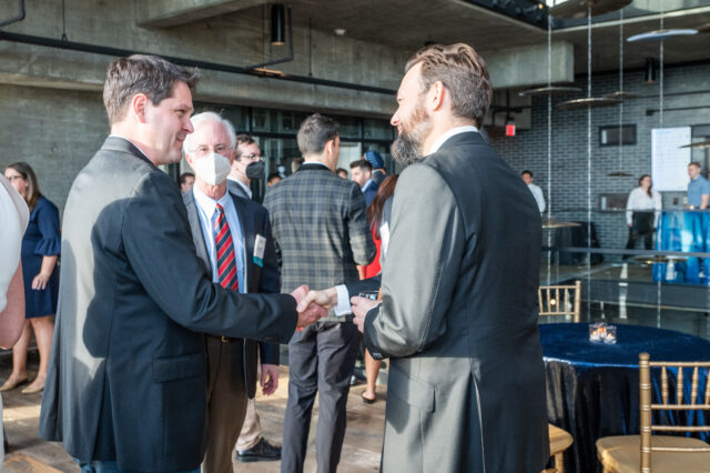 Guests at CDT's 2022 Tech Prom, two shaking hands while another is wearing a mask.