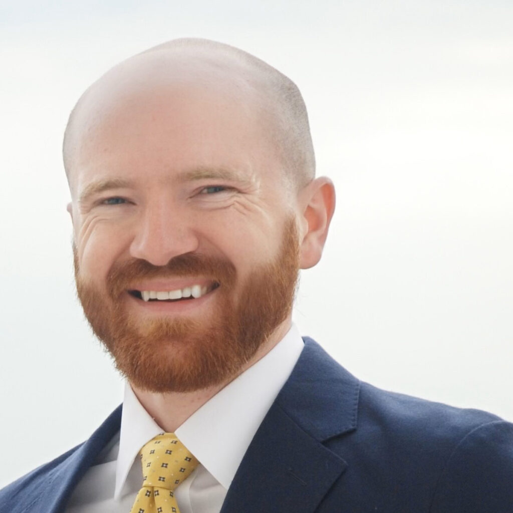 Kevin Donnelly, smiling outside with a beard while wearing a blue suit and yellow tie.