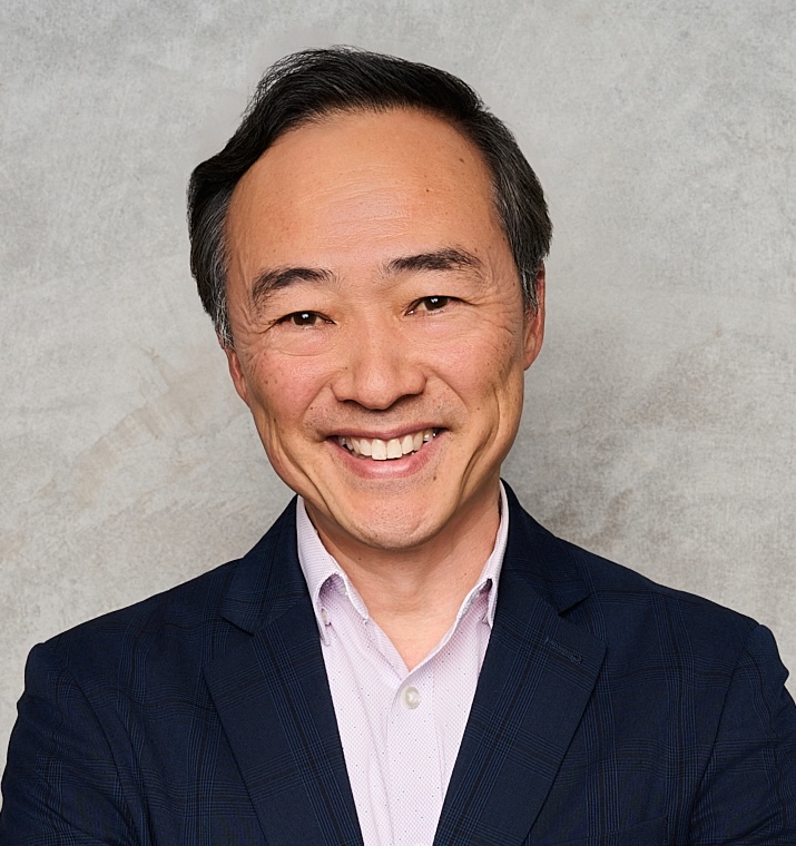 Chan Park, smiling in a collared shirt and dark suit jacket, in front of a grey backdrop.
