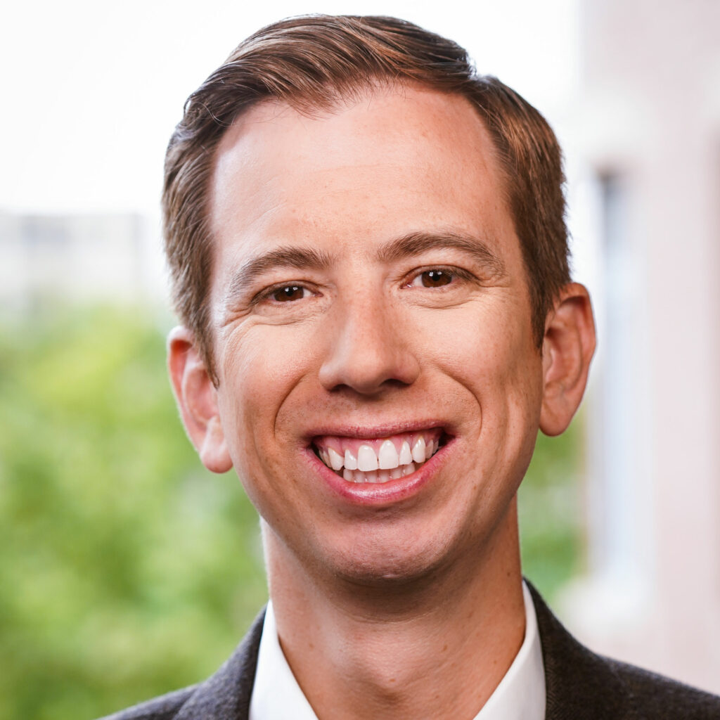 Drew Courtney. CDT's Director of Communications. Headshot image of man in front of greenery.