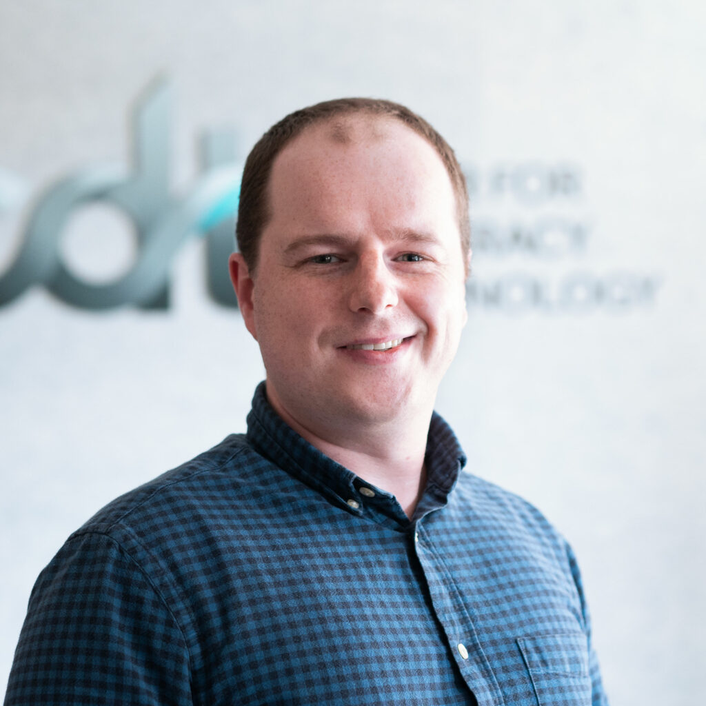 Jacob Kauffman, smiling and wearing a patterned collared shirt in front of the CDT logo.