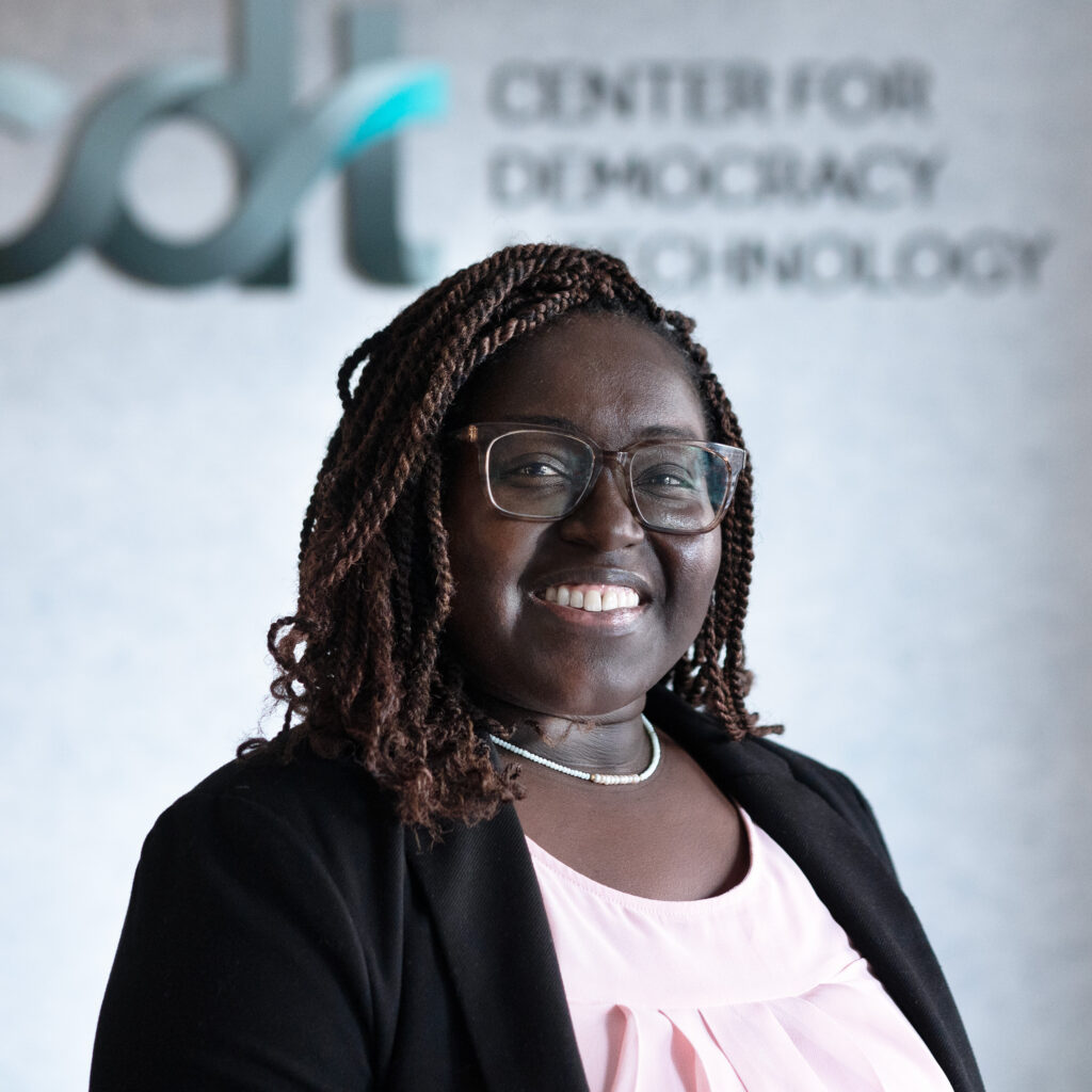 DeVan Hankerson Madrigal, smiling and wearing glasses and a pink top and black suit jacket.