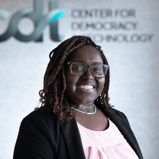 DeVan Hankerson Madrigal, smiling and wearing glasses and a pink top and black suit jacket.