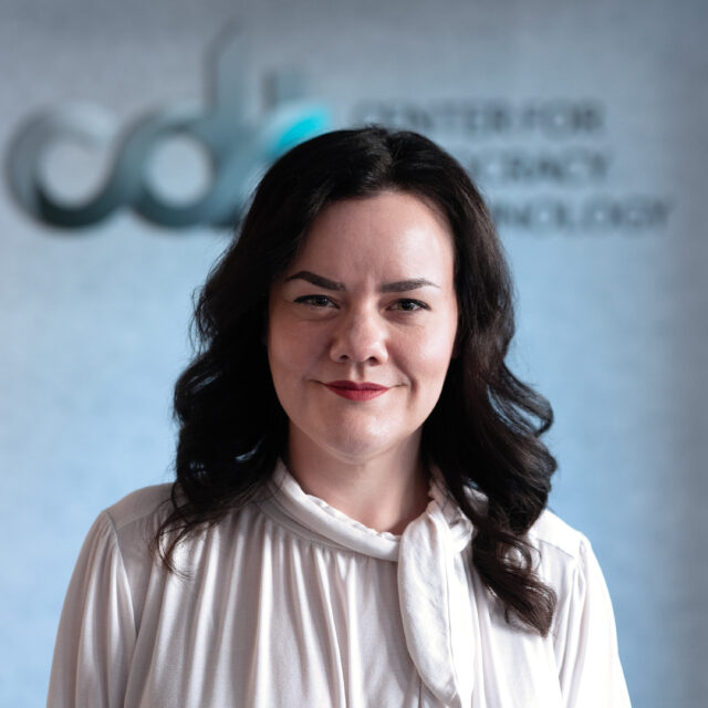 Becca Barnum, smiling in front of the CDT logo, wearing red lipstick and a white textured top.
