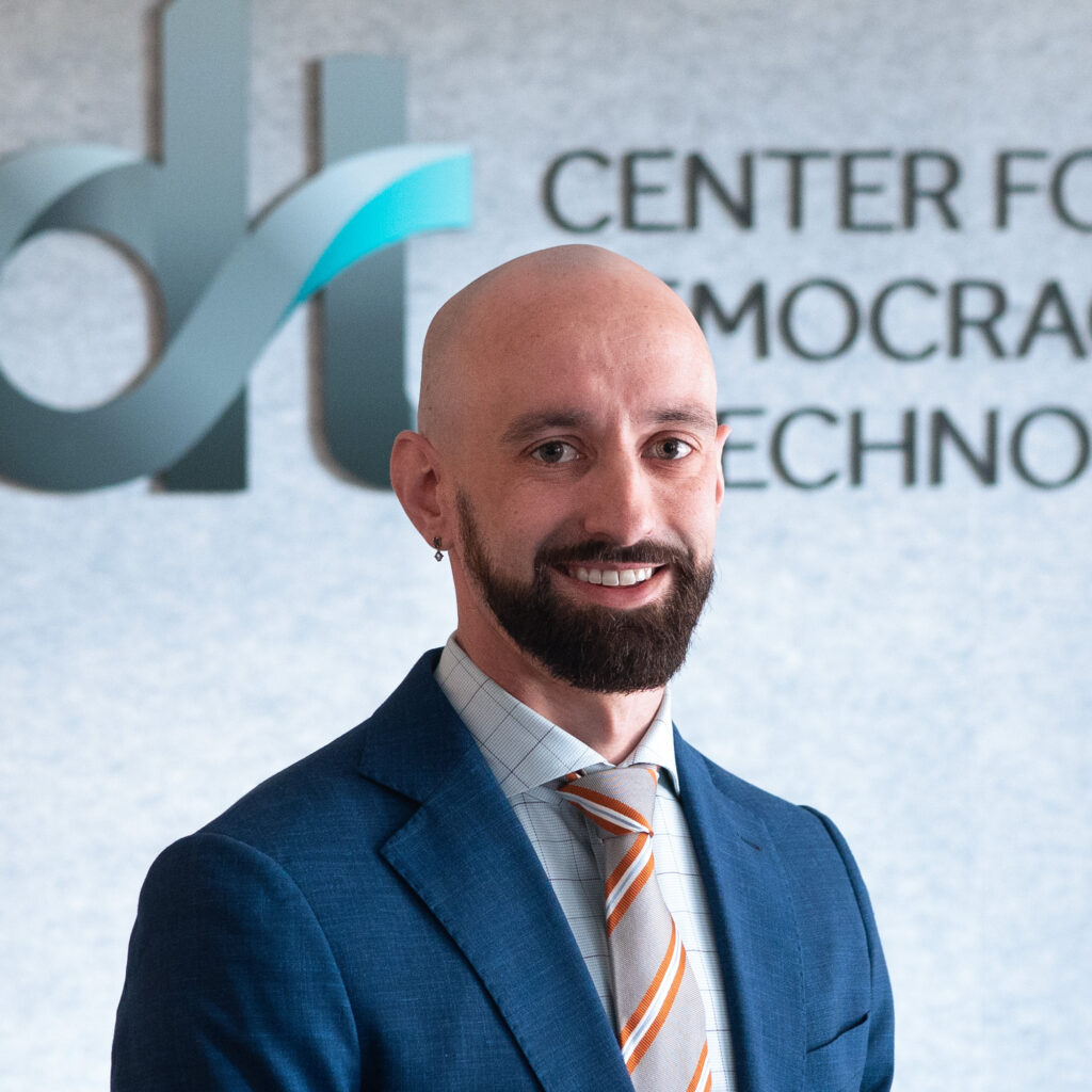 Tom Bowman, smiling in a blue suit and collared shirt and tie, in front of a CDT logo.