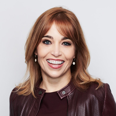 Erin Egan. Meta Platforms, Inc. Wearing a burgundy shirt and leather jacket, in front of a light colored backdrop.