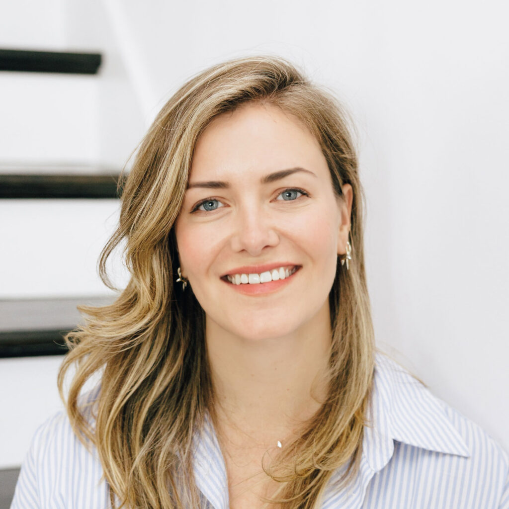 Liza Getsinger, smiling in white collared shirt, sitting on a white and dark brown wooden staircase.