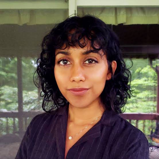 Irene Solaiman, wearing a dark top in front of a reflection of a green outdoor setting.
