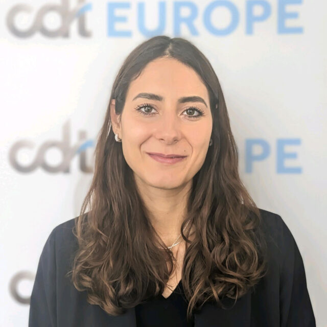Joanna Tricoli, smiling in a black jacket, standing in front of a CDT Europe backdrop.
