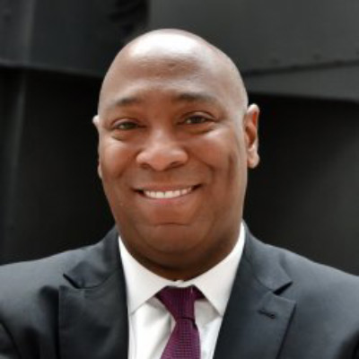 Roscoe Jones. Gibson, Dunn & Crutcher. Wearing a white collared shirt and dark suit, in front of a dark grey building.