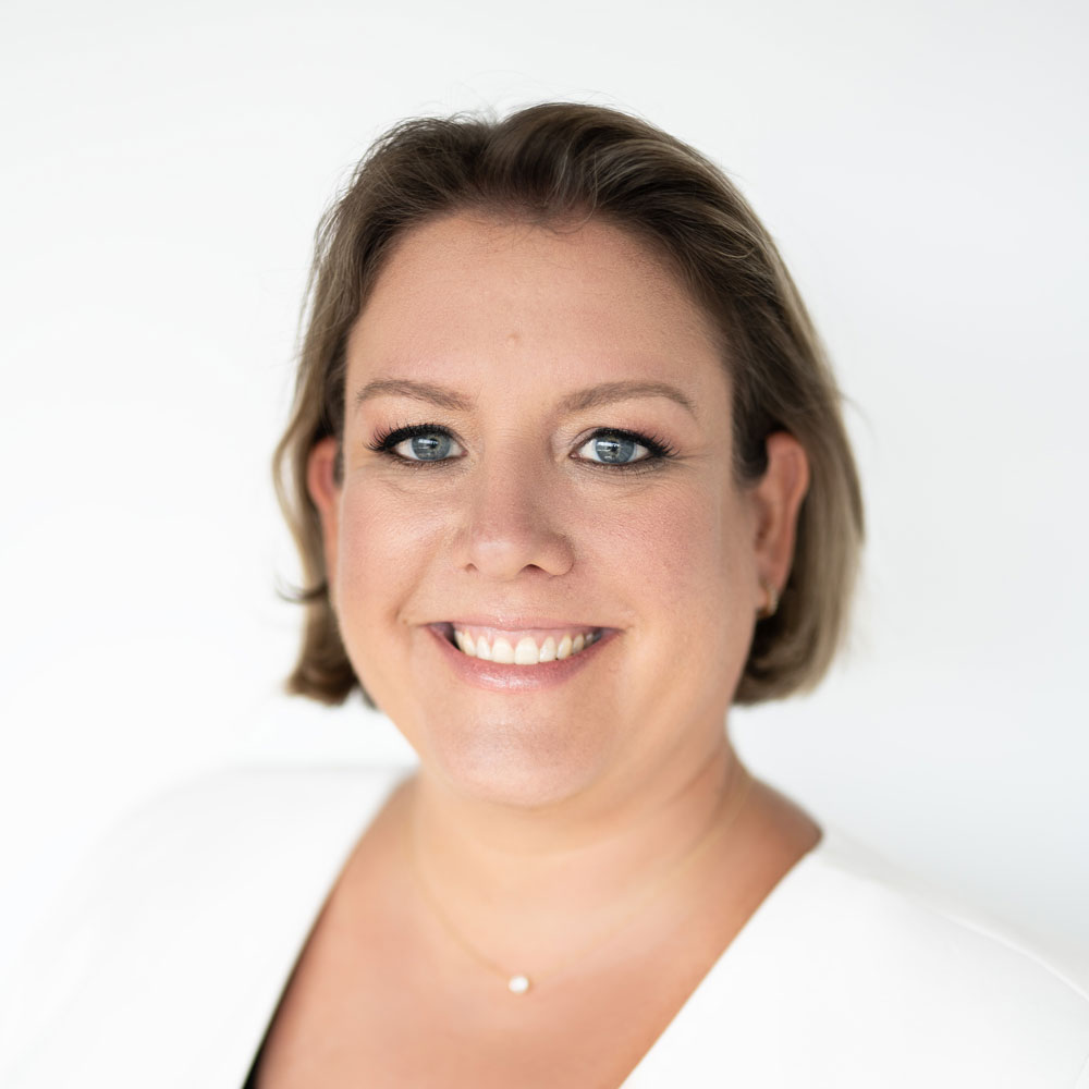 Katie Harbath, wearing white and smiling in front of a white background.