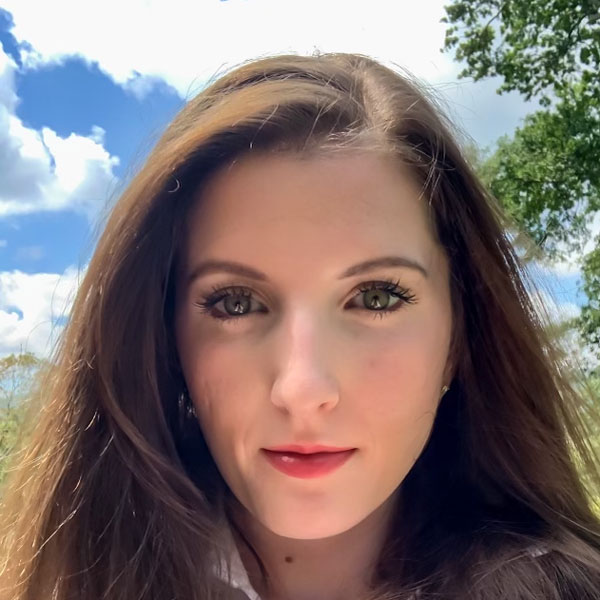 Kendal Aldridge, standing in front of a bright blue sky and a green outdoor setting.