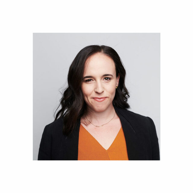 Miranda Bogen, wearing a burnt orange top and black jacket, smiling in front of a grey background.
