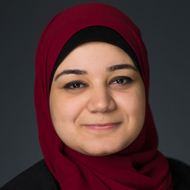Mona Elswah, wearing a dark red headscarf and a black jacket while smiling.