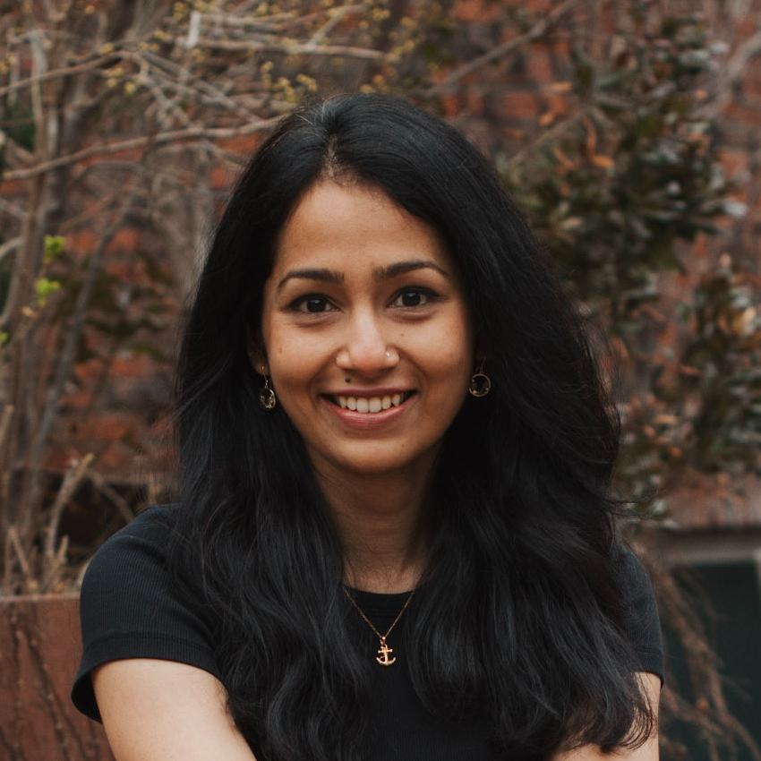 Ruchika Joshi, smiling wearing a black top and necklace in front of a fall outdoor background.