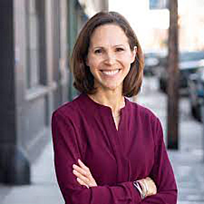 Alissa Starzak. Cloudflare. Wearing a deep purple shirt in front of a grey background.