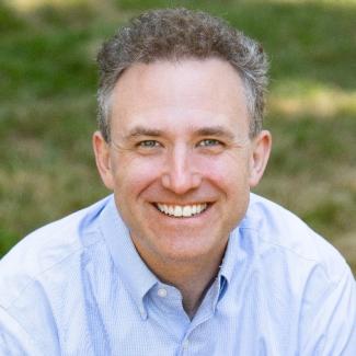 Travis Hall, smiling in a collared shirt outdoors.