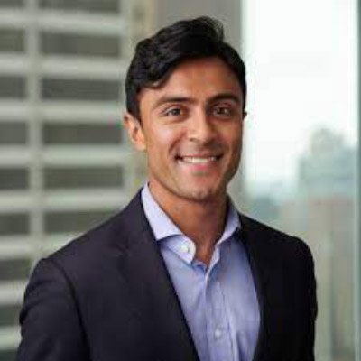 Vinay Trivedi. General Atlantic. Wearing a light blue collared shirt and a dark suit, in front of a grey background.