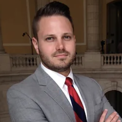 Chris Wood, wearing a grey suit and red and black tie.