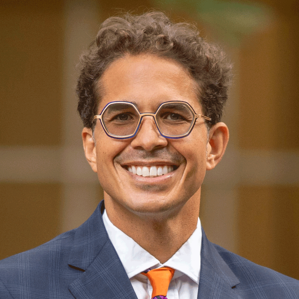 Paul Gowder, smiling wearing round glasses, a gray suit and yellow tie.