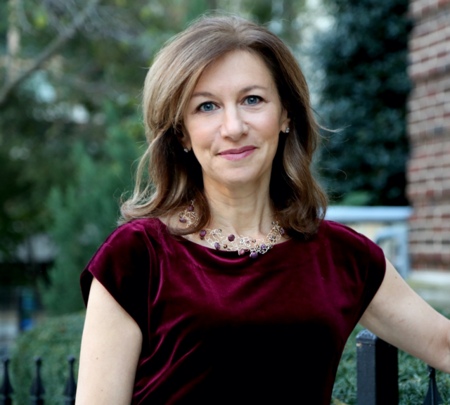 Photograph of Karen Kornbluh, smiling outdoors wearing a burgundy velvet top and gold necklace.