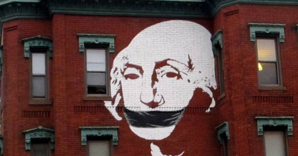 Mural of a stylized face with a black band over the mouth on a red brick building.